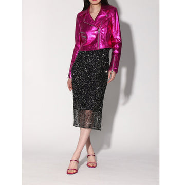 A woman standing wearing a metallic pink cropped leather jacket with a spread collar and front zipper details, paired with a black skirt with fringe details.