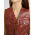 A close-up of a model wearing a rust-brown leather vest with two front flap pockets and metal snap buttons, set against a plain light gray background.