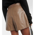 Model styling women’s chic brown leather high-waisted shorts with a white blouse and heels for a modern outfit.